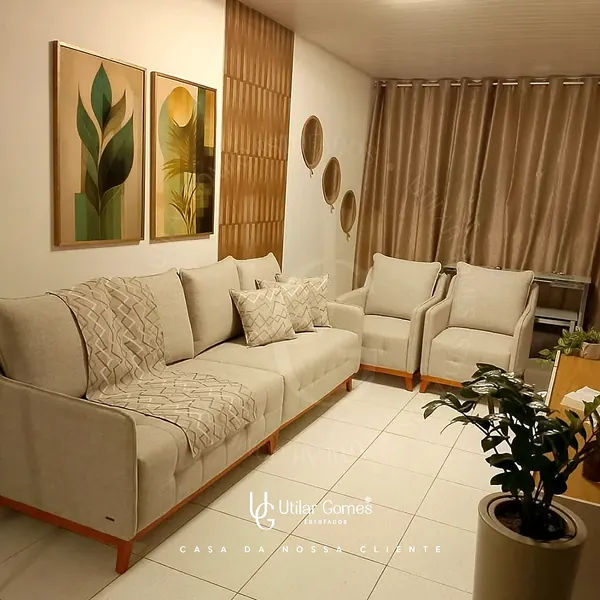Sala com sofá e duas poltronas claras, quadros e painel de madeira
