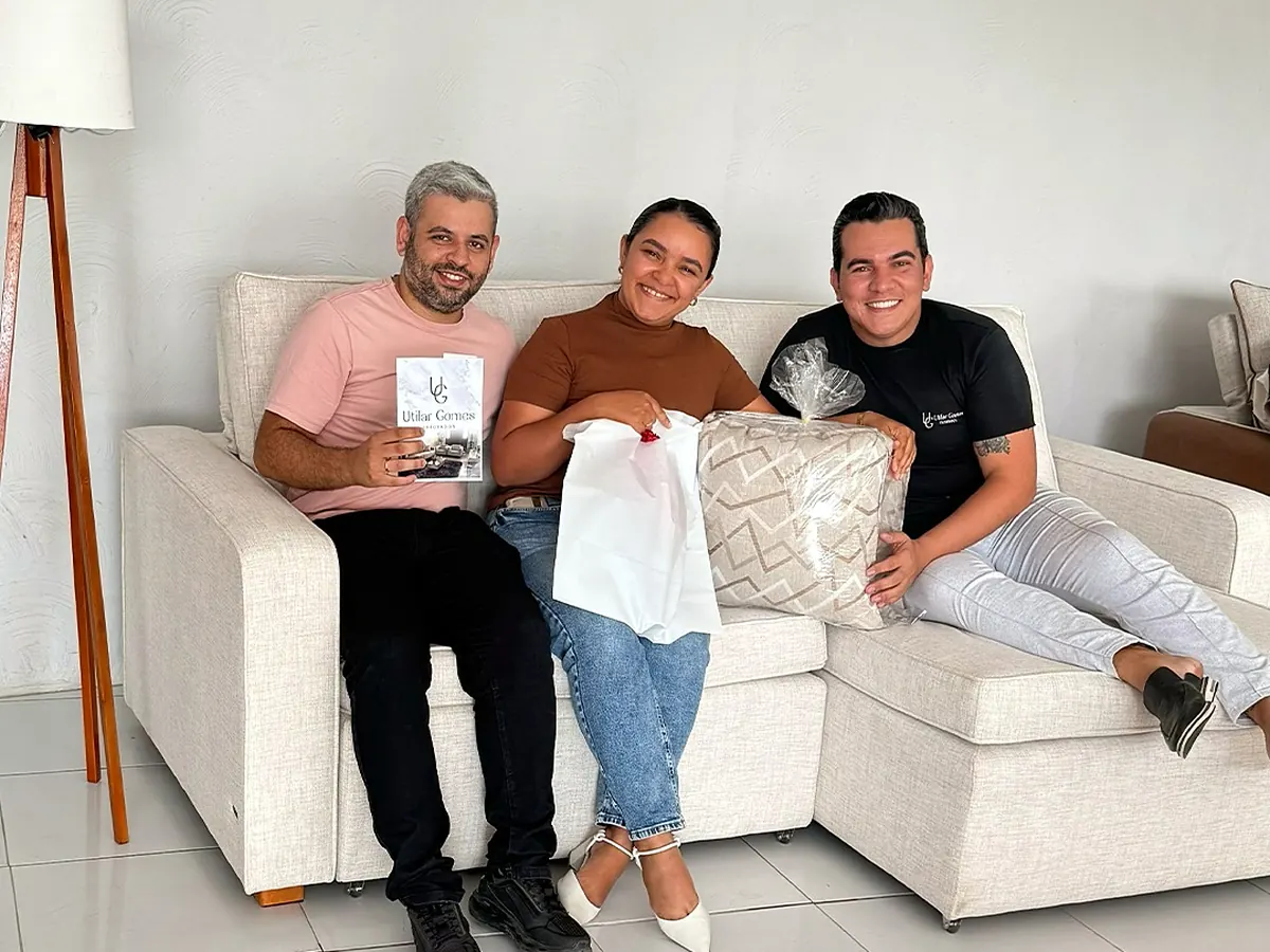 Clientes sorrindo em sofá claro da Utilar Gomes, segurando o folder da marca
